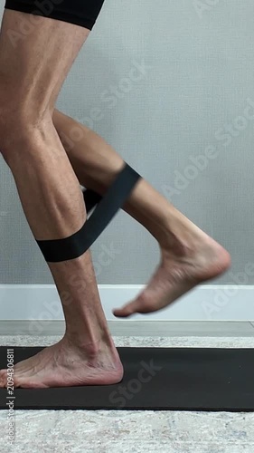 Muscular man performing leg extension exercises with a resistance band. Home workout for strengthening glutes, hamstrings, and calves