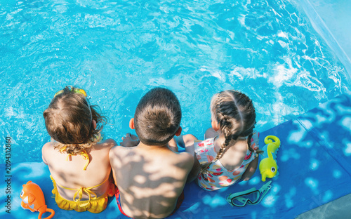 Three children sitting together by swimming pool, back view
