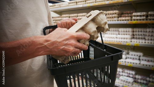 Foto Close-up of a customer's hand putting a carton of eggs into a grocery basket in a supermarket egg aisle