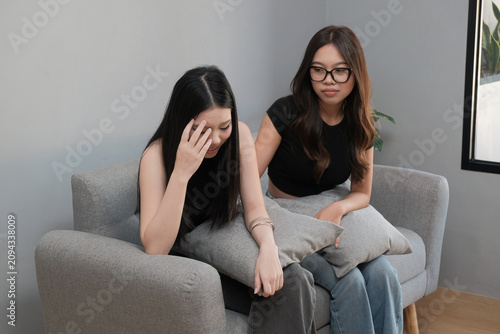 Young Asian Woman Comforting a Sad Friend Sitting on a Sofa at Home