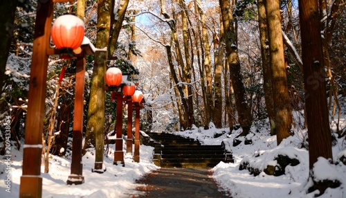 Snow-covered path lined with red lanterns in a forest, leading to stone steps