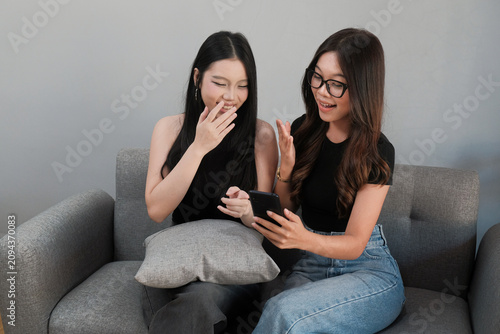 Happy Young Asian Women Looking at Smartphone Together on Sofa at Home
