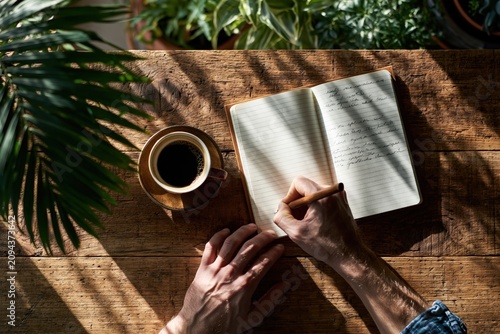 Person writing in a journal on a wooden desk early morning li