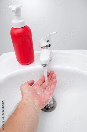 Washing Hands Under Running Water with Foaming Soap in a Clean White Sink