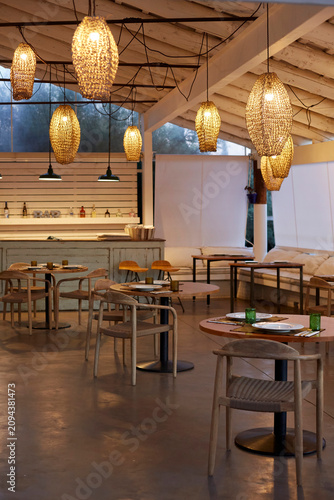 Luxury mediterranean restaurant interior with wooden furniture and decorative wicker pendant lamps