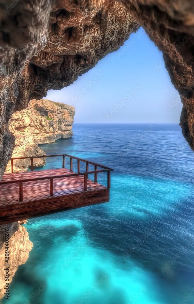 Fototapeta premium A serene ocean view from a rocky cave with a wooden dock