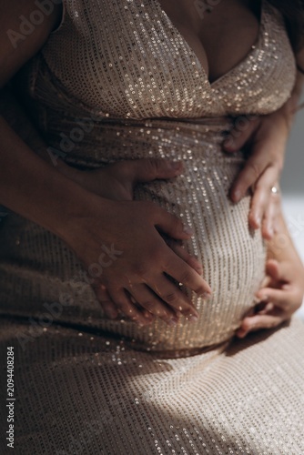 Close-up view of couple hands hugging pregnant woman belly in sequin dress