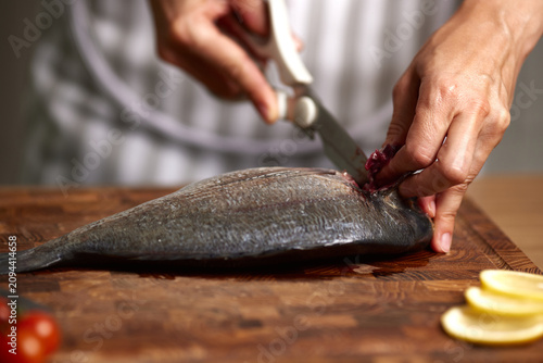 Obraz na płótnie Hands cutting fresh raw sea bream on wooden board