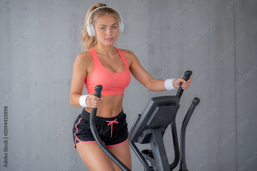 Fototapeta premium Kobieta wykonuje trening cardio na orbitreku w siłowni, ćwicząc z wykorzystaniem ruchomych uchwytów urządzenia.