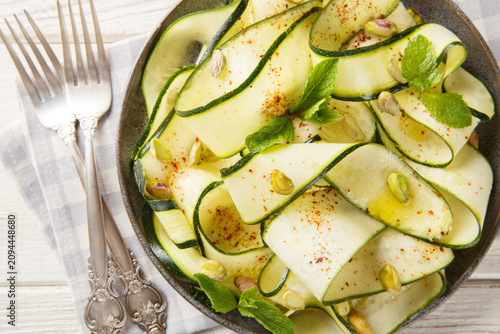 Gourmet zucchini ribbon salad with pistachios, chili pepper and mint, elegant vegetable appetizer close-up in a plate on the table. Horizontal top view from above