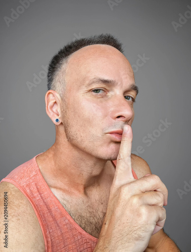 Middle-aged man making a shush gesture with finger on lips, studio portrait