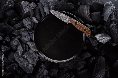 Damascus steel fixed blade knife on a black plate over dark charcoal.