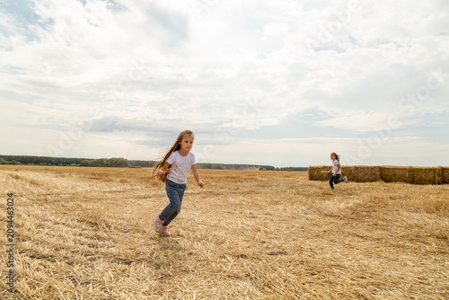 Sisters having fun in a wheat field on a summer day. Children playing at hay bale field during harvest time.