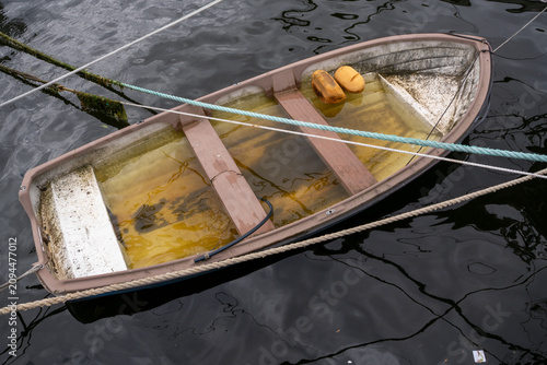 Fotografie tied weathered rowboat filled with shallow murky water and almost sinking