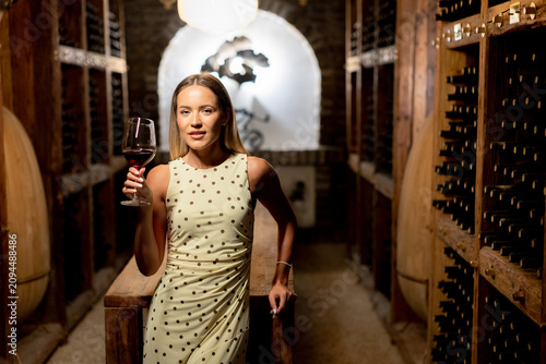 Elegant woman enjoys red wine in a charming wine cellar during evening hours