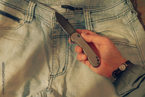 Male hand holding a pocket knife against a denim background.