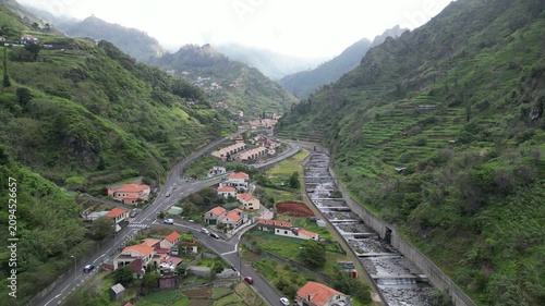 Aerial pull-away shot moving through Sao Vicente mountain valley with village and river