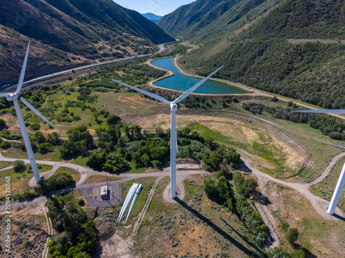 Aerial view of wind turbines in a lush canyon near a blue reservoir