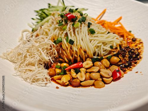 close-up of Chinese cold noodles shows tender shredded chicken, crunchy peanuts and green cucumbers in spicy chili oil