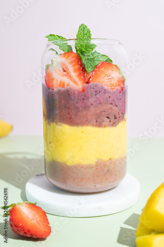 Close up of colorful berry smoothie served in a glass with fresh strawberry garnish.