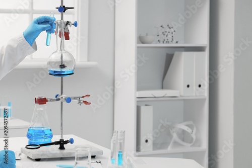Scientist in blue gloves holding a test tube with blue liquid over a laborato...