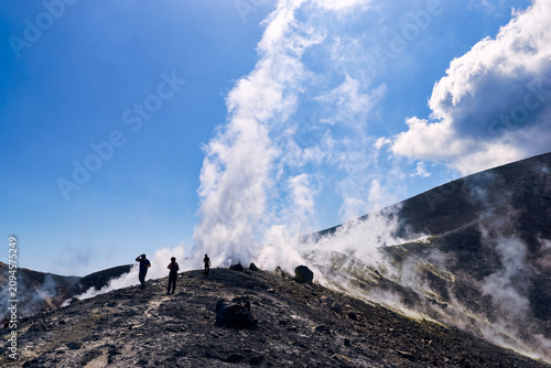 Hikers exploring active volcanic crater rim with smoking fumaroles on Vulcano island, Italy