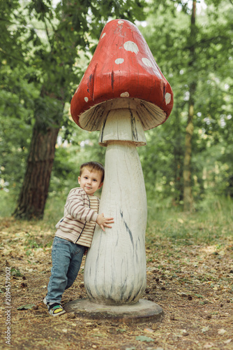 Cute little boy hugging a huge decorative wooden mushroom in forest