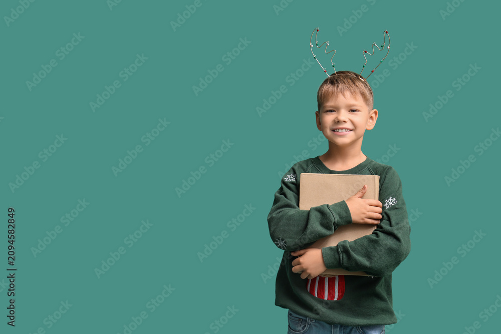 Obraz premium Cute little boy in Christmas reindeer horns with book on green background