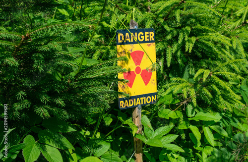 Obraz na płótnie Yellow radiation warning sign with the word Danger hidden in dense green forest bushes