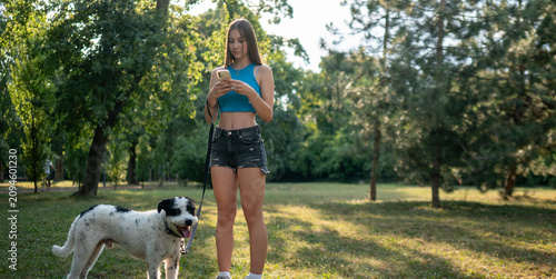 Teen girl checking smartphone while walking her mixed breed dog at sunset
