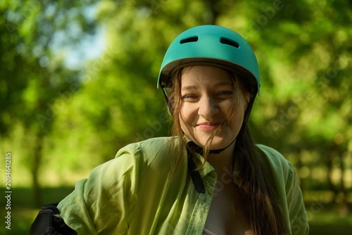 Smiling girl wears a helmet and green shirt in park during sunny day while enjoying outdoor activity with friends
