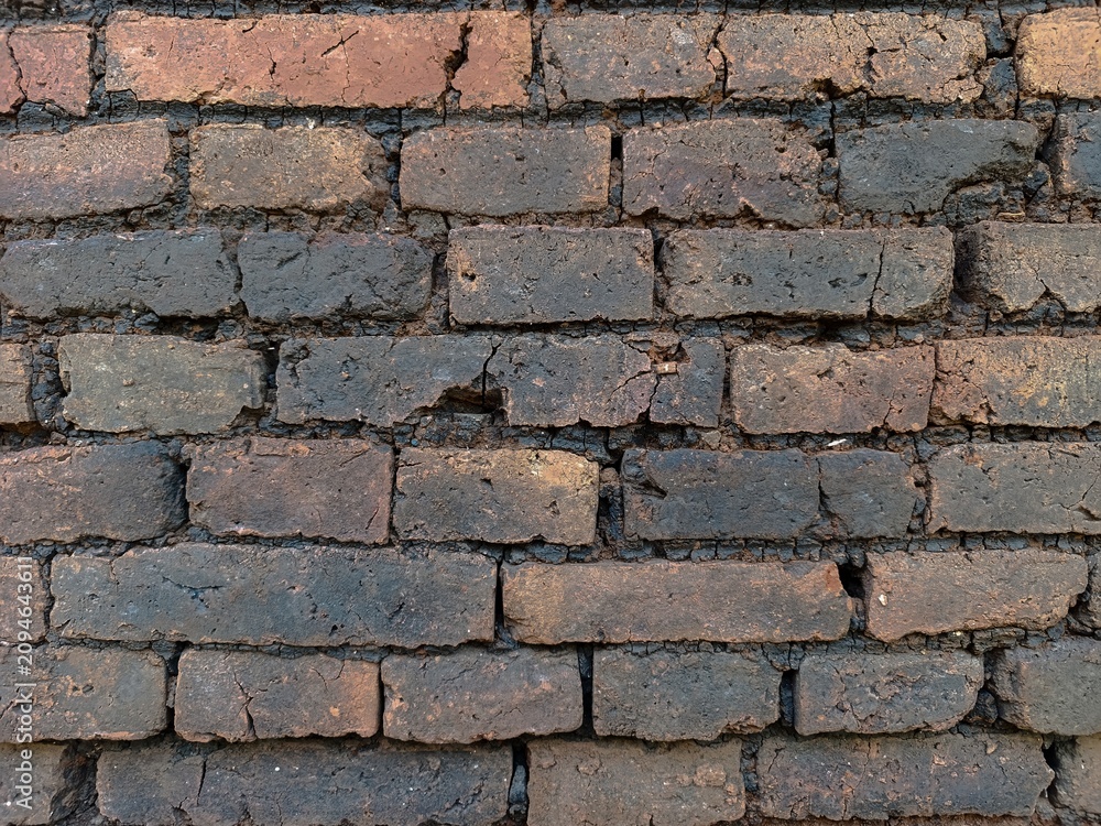 Obraz premium Close-up of an old weathered brick wall with cracked clay bricks and rustic masonry texture, ideal as an authentic architectural background or construction design element.
