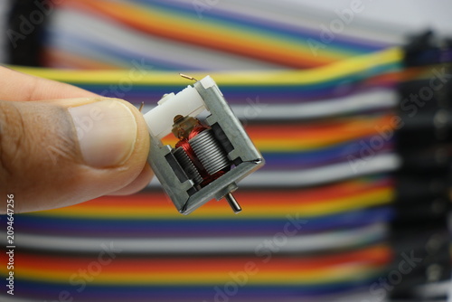 Open frame dc motor with visible shaft and copper windings used for electronic and diy projects held in the hand