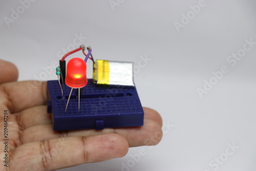 Small breadboard with glowing red LED powered by lithium polymer battery held in the hand