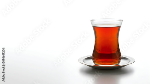 Refreshing amber colored hot tea in traditional curved glass on saucer white background with soft shadows and copy space.