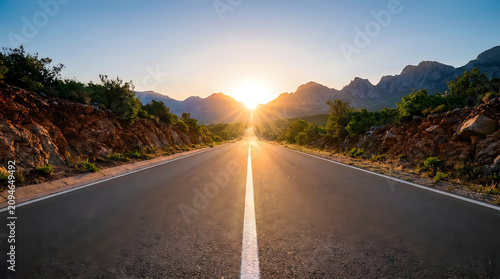 Sunrise over mountain range with sun rays shining through clouds onto empty asphalt road stretching towards horizon, journey and hope concept.