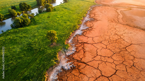 Aerial view showing stark contrast between lush green riverside landscape and arid cracked dry desert earth representing environmental change and global climate change impact.