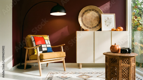Cozy modern living room corner with armchair, floor lamp, and decorative cabinet, featuring autumnal accents like pumpkins and botanical art, creating inviting ambiance.