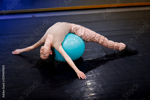 Dancer performs an exercise routine on a blue stability ball in a studio during a training session in the afternoon