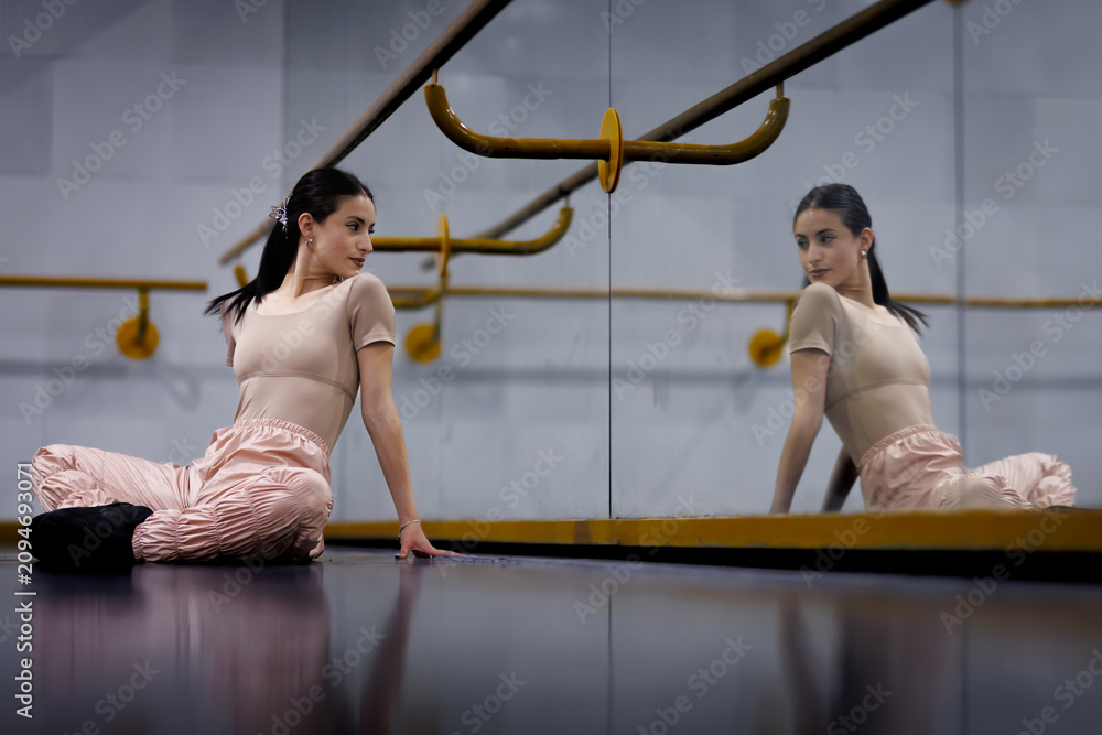 Fototapeta premium Dancer sits on the floor in front of a mirror during a practice session at a dance studio in the afternoon