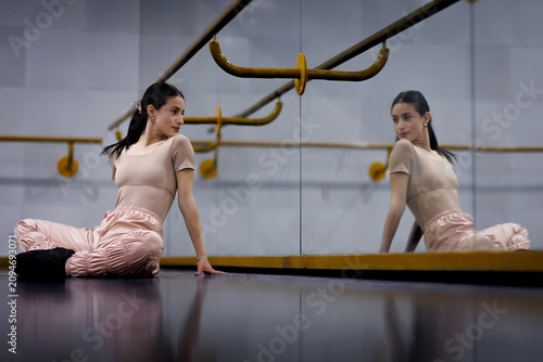 Dancer sits on the floor in front of a mirror during a practice session at a dance studio in the afternoon