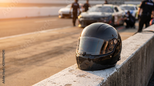 Carbon fiber racing helmet resting on a concrete pit wall during sunset with blurred cars in the background