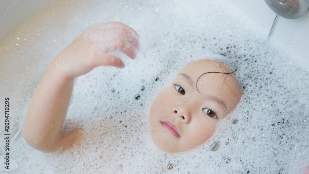 Fototapeta premium A curious young child unwinds in a bathtub full of bubbles, immersed in a peaceful sensory experience as part of a calming daily bathtime routine at home.