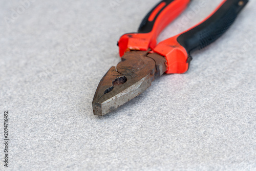 Rusty combination pliers with red and black handle on gray background