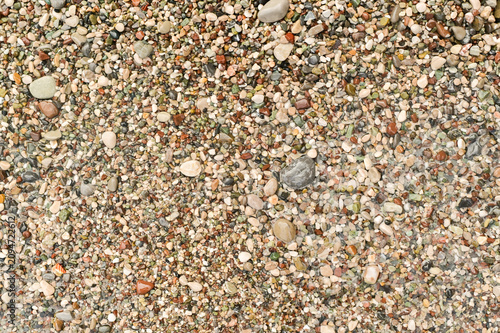Small pebbles cover sea beach surface. Natural stone texture creates beautiful background for summer design. Multicolored gravel patterns provide abstract look on sandy shore.