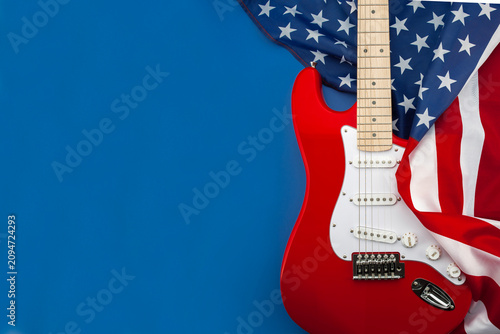 Red electric guitar with American flag on blue background. Patriotic music concept inspired by rock culture, live performance and American entertainment with copy space