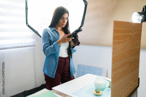 Young woman working as a professional product photographer  adjusting her camera in a studio with softbox lighting