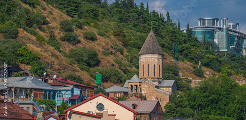 Architectural contrast in old Tbilisi with ancient church and modern glass mansion
