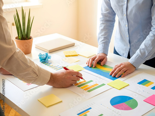 Business professionals analyzing colorful financial charts and graphs on paper during a collaborative meeting in a bright office space with professionals working together