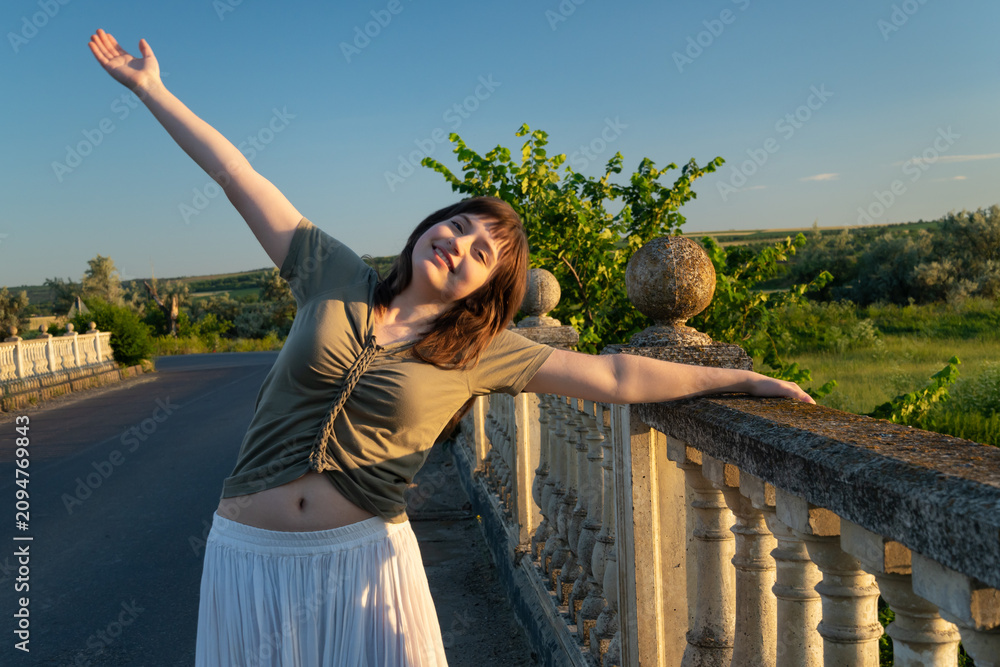 Obraz premium Happy young woman enjoying freedom on a stone bridge at sunset
